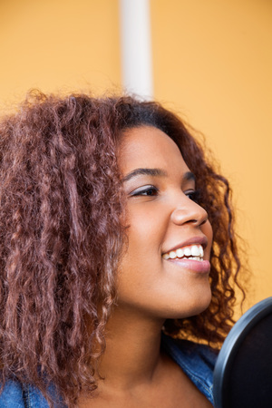 Closeup of young woman with curly hair singing in recording studioの写真素材