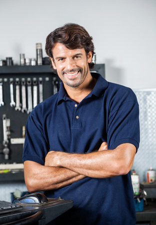Portrait of happy male mechanic standing arms crossed in auto repair shopの写真素材