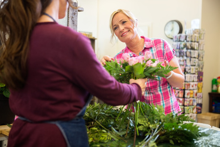 Happy mature woman buying bouquet of roses from florist in shopの写真素材