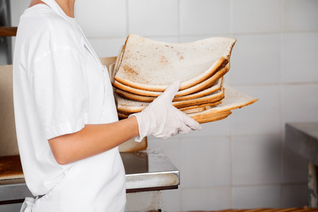 Side view midsection of female baker holding bread waste in bakeryの写真素材