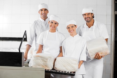 Portrait of confident male and female Baker's with packed breads in bakeryの写真素材