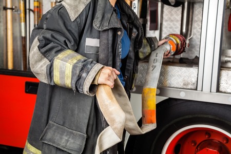 Midsection of firewoman adjusting water hose in truck at fire station