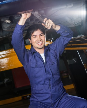 Portrait of happy male mechanic repairing underneath car at auto repair shopの写真素材