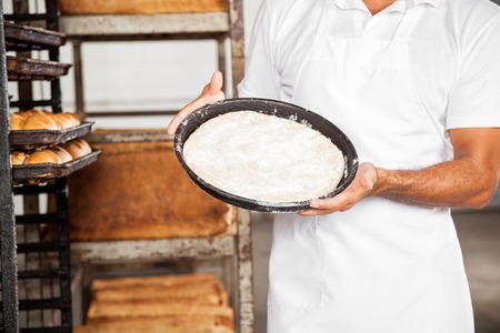 Midsection of male baker showing dough tray at bakeryの写真素材