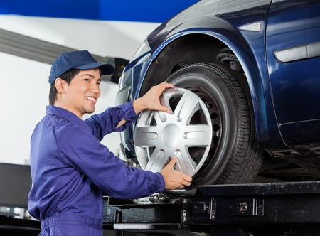 Smiling young mechanic fixing alloy to car tire at garage Smiling young mechanic fixing alloy to car tire at garage