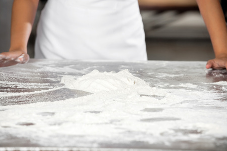 Closeup of dough on table with female baker standing in bakery