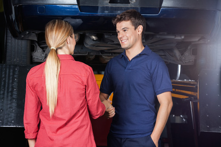 Smiling male mechanic shaking hand with customer at auto repair shopの写真素材