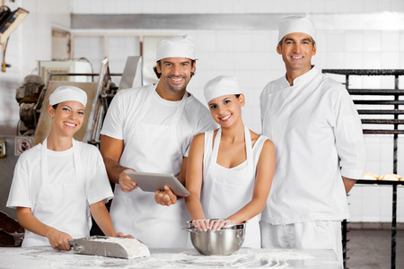 Portrait of confident male and female Baker's with digital tablet together at table in bakery
