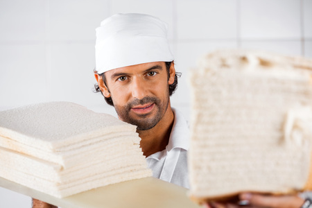 Portrait of confident male baker with bread slices in bakeryの写真素材