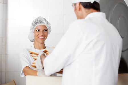 Smiling female baker receiving bread waste from male colleague in bakeryの写真素材