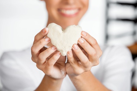 Midsection of young female baker holding heart shape dough in bakeryの写真素材