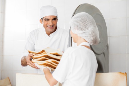 Happy male baker receiving bread waste from female coworker in bakeryの写真素材