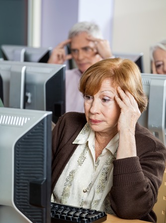 Tensed senior female student looking at computer while sitting in classroomの写真素材