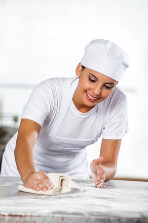 Smiling female baker cleaning table in bakery