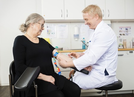 Mature male doctor collecting senior patient's blood for test in hospitalの写真素材