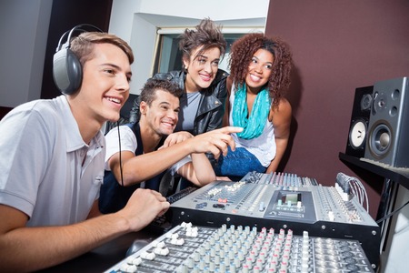 Happy multiethnic musicians mixing audio together at table in recording studio