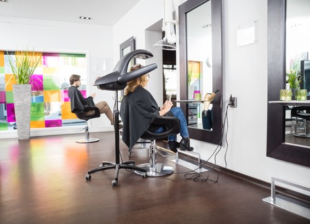 Male and female customers undergoing hair treatment in salonの写真素材