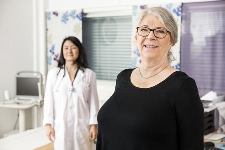 Portrait of smiling senior patient standing with doctor in background at clinicの写真素材