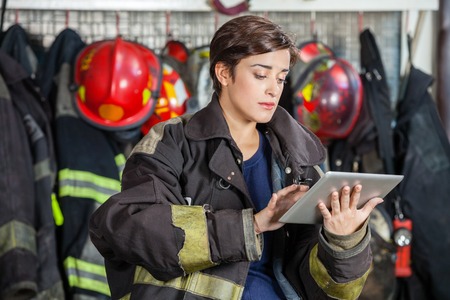 Confident firewoman in uniform using digital tablet at fire station