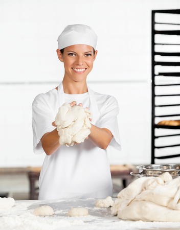 Portrait of happy female baker showing dough at table in bakery