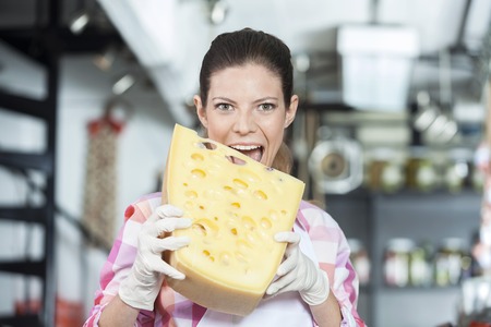 Portrait of young saleswoman biting cheese in store