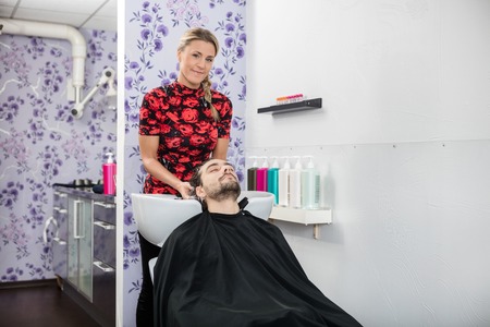 Portrait of confident female hairdresser washing male customer's hair in salonの写真素材