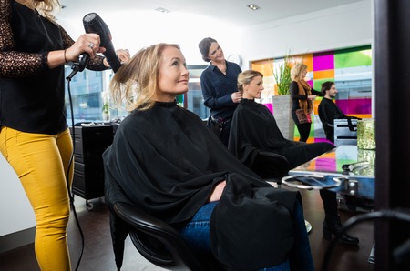 Male and female hairdressers setting client's hair in salon