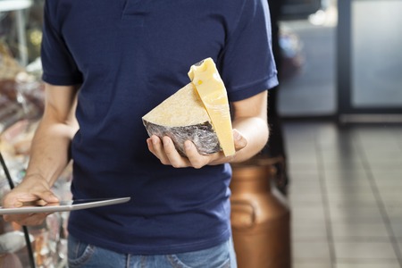 Midsection of young man holding cheese and digital tablet in grocery storeの写真素材