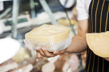 Midsection of salesman holding cheese pieces in shopの写真素材