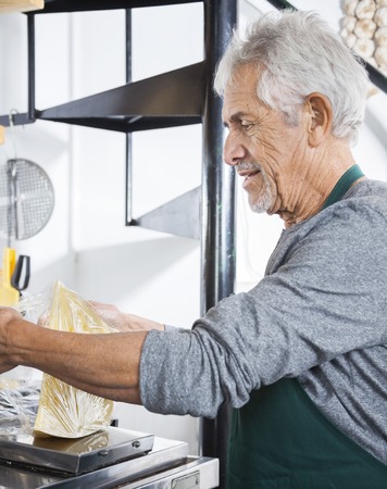 Side view of senior salesman packing cheese at grocery storeの写真素材