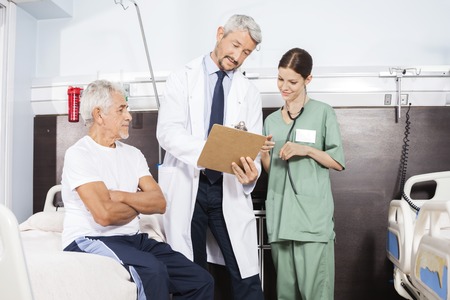 Mature male doctor and nurse communicating over report by senior patient in rehab centerの写真素材