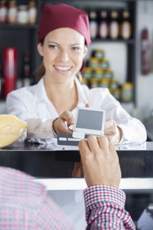 Male customer swipes his credit card to make payment in cheese shop
