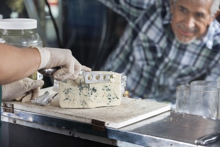 Senior man watching salesman slicing blue cheese at counter in shopの写真素材