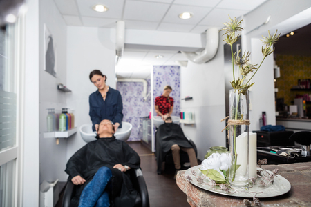 Flower vase on table in salon with hairdressers washing customers hair in backgroundの写真素材