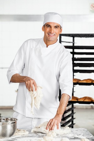 Portrait of confident male baker kneading dough at table in bakeryの写真素材