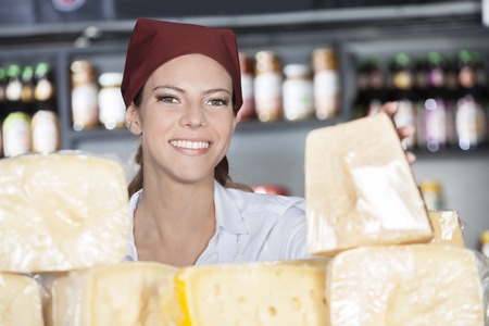 Portrait of happy young woman selling fresh cheese in storeの写真素材