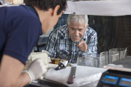 Happy senior man selecting cheese from display cabinet in shopの写真素材