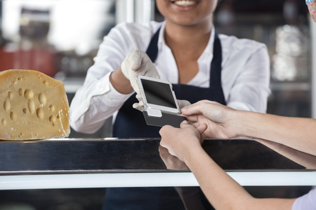 Cropped image of young woman making payment through credit card at cheese shop