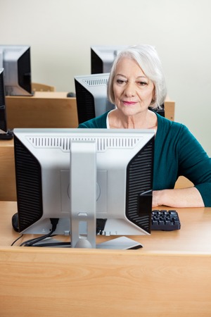 Senior female student using computer at desk in classroom