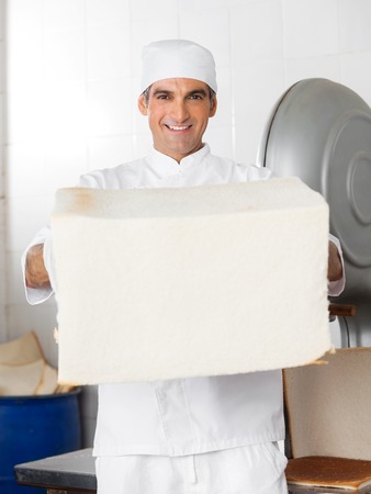 Portrait of confident male baker holding big bread loaf in bakeryの写真素材