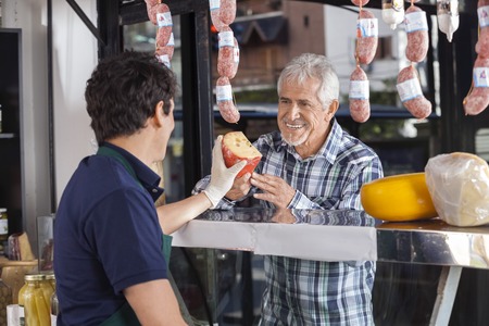 Happy senior man buying cheese from salesman in shopの写真素材