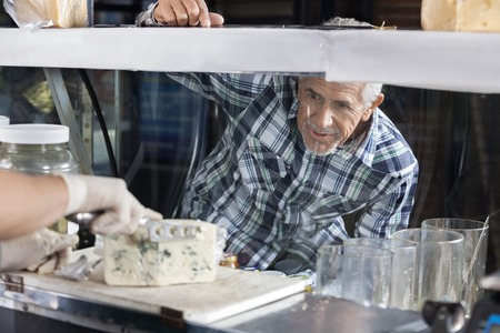 Senior man watching salesman slicing blue cheese at counter in shopの写真素材