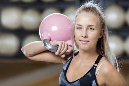 Portrait of confident young woman lifting kettlebell in gymの写真素材