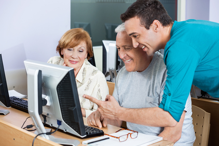 Young male tutor assisting senior students in using computer at classの写真素材