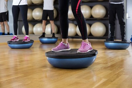 Low section of male and female friends standing on bosu ball in gymの写真素材