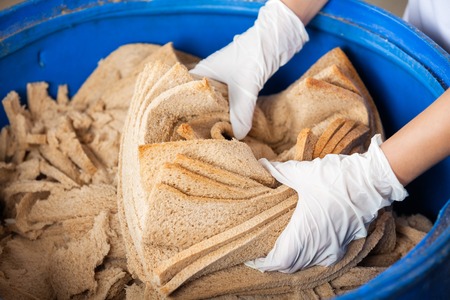 Closeup of female baker's hands discarding bread waste in garbage bin at bakeryの写真素材
