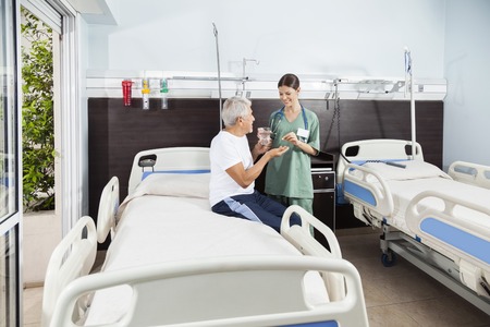 Smiling nurse giving medicine and water to senior patient in rehabilitation centerの写真素材