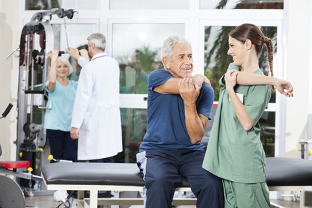 Smiling female nurse guiding senior patient in arm exercise at rehab fitness centerの写真素材