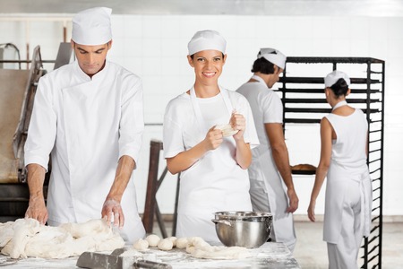 Portrait of smiling female baker kneading dough with colleague in bakeryの写真素材