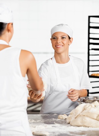 Smiling female baker giving dough to colleague in bakeryの写真素材